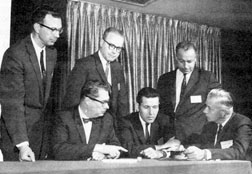 Speakers at IPC's Fall Technical Symposium. Seated left to right: W.D. Fuller, Lockheed Electronics Co.; J. M. Rausch, Bell Telephone Laboratories; and Oscar Vance, Burroughs Corp. Standing: D.F. Pennie, Remington Rand Univac Division; G.B. Devey, Spraugue Electric Co.; and R.G. Zensa, Elecrtalab Printed Electronics Inc.